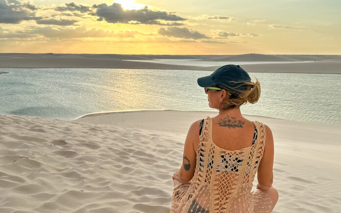 Erros ao viajar sozinha pela primeira vez mulher em viagem solo feminina contemplando dunas ao pôr do sol refletindo sobre erros na primeira viagem sozinha