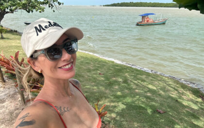 Mulher em viagem solo aproveitando a praia com barco ao fundo (Tatiana Prata)